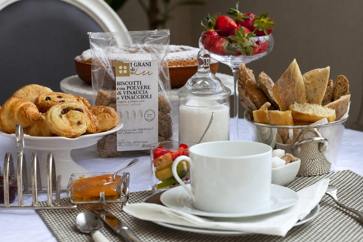 Colazione con biscotti alla polvere di vinaccia e vinaccioli I Grani di Lu, accompagnati da caffè, pane, fragole e prodotti da forno.