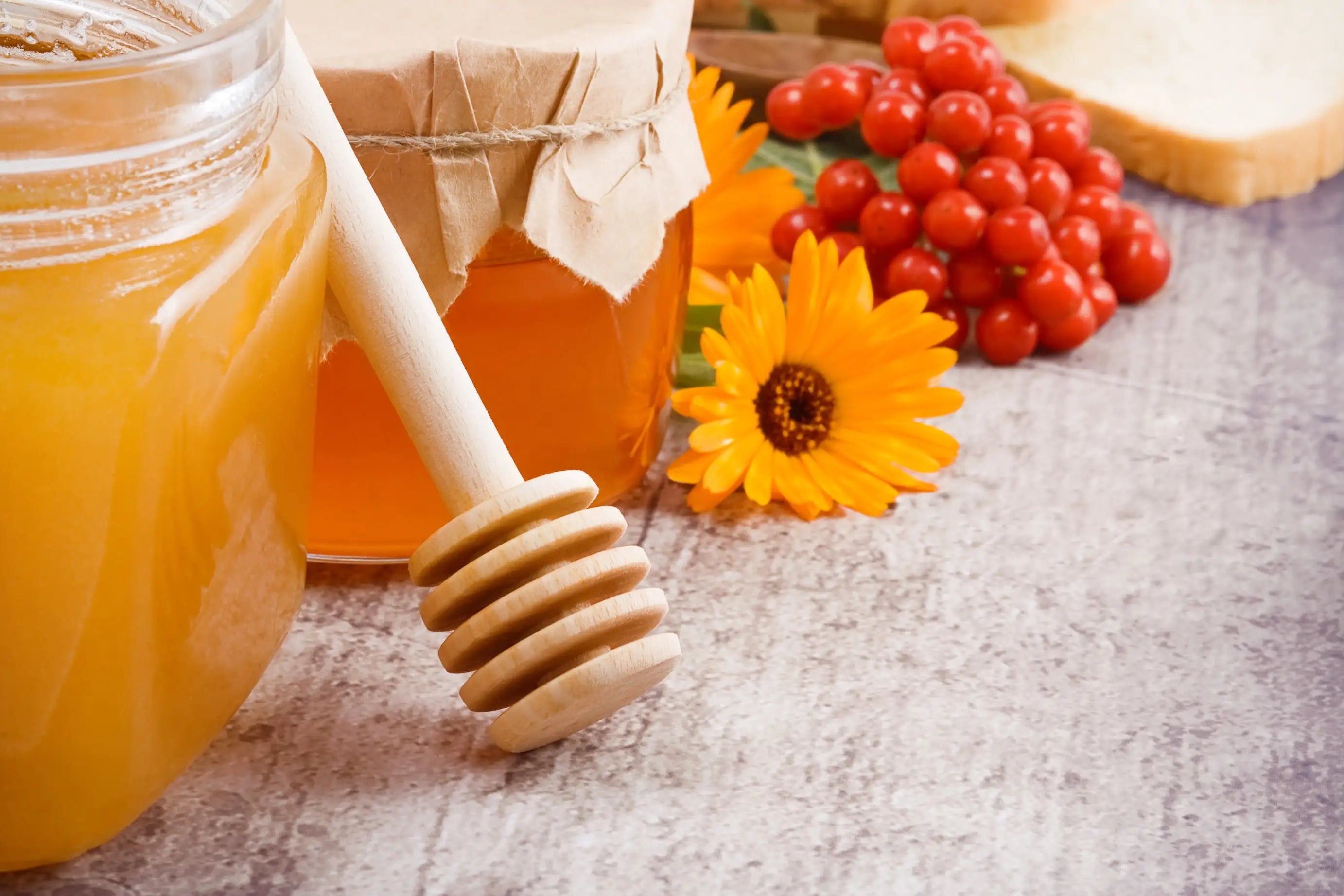 Miele artigianale in barattoli di vetro con mestolo in legno, fiori decorativi e bacche rosse