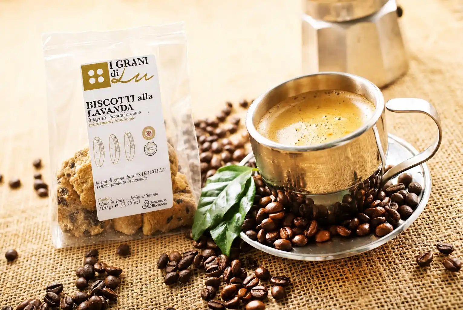 Confezione di biscotti integrali alla lavanda I Grani di Lu accanto a una tazza di caffè e chicchi di caffè.