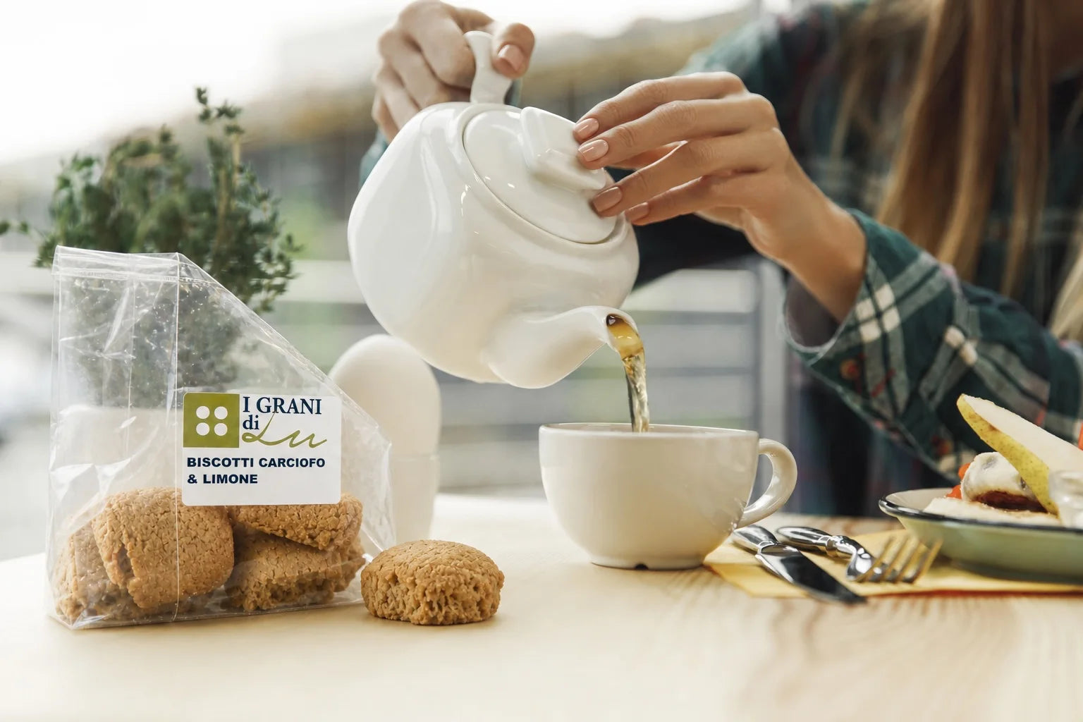 Confezione di biscotti al carciofo e limone I Grani di Lu accanto a una tazza mentre viene versato il tè.