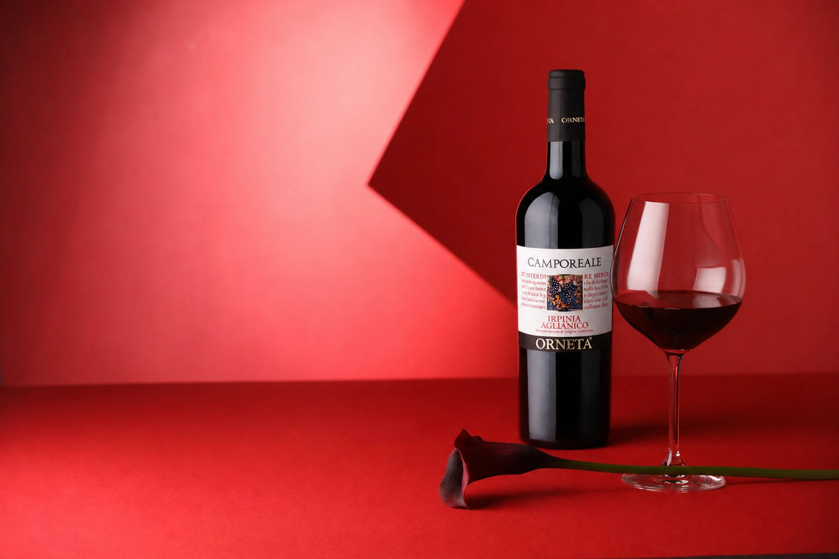 Bottiglia di Camporeale Irpinia Aglianico DOC Orneta accanto a un calice di vino rosso su sfondo rosso.
