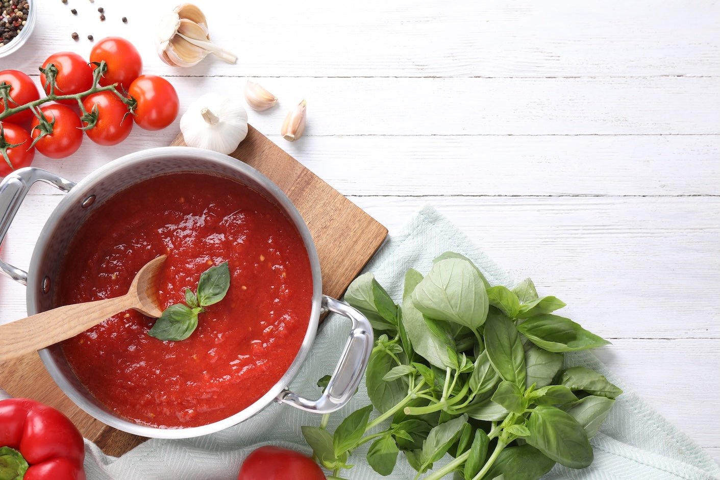 Salsa di pomodoro con basilico fresco, aglio e pomodorini, preparata su piano chiaro da cucina.