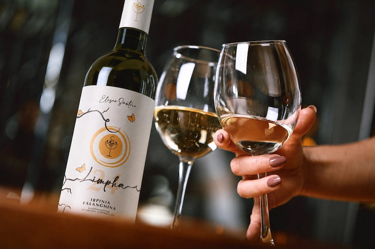 Bottiglia di Limpha Irpinia Falanghina DOC di Eliseo Santoro accanto a due calici di vino bianco, uno tenuto in mano.