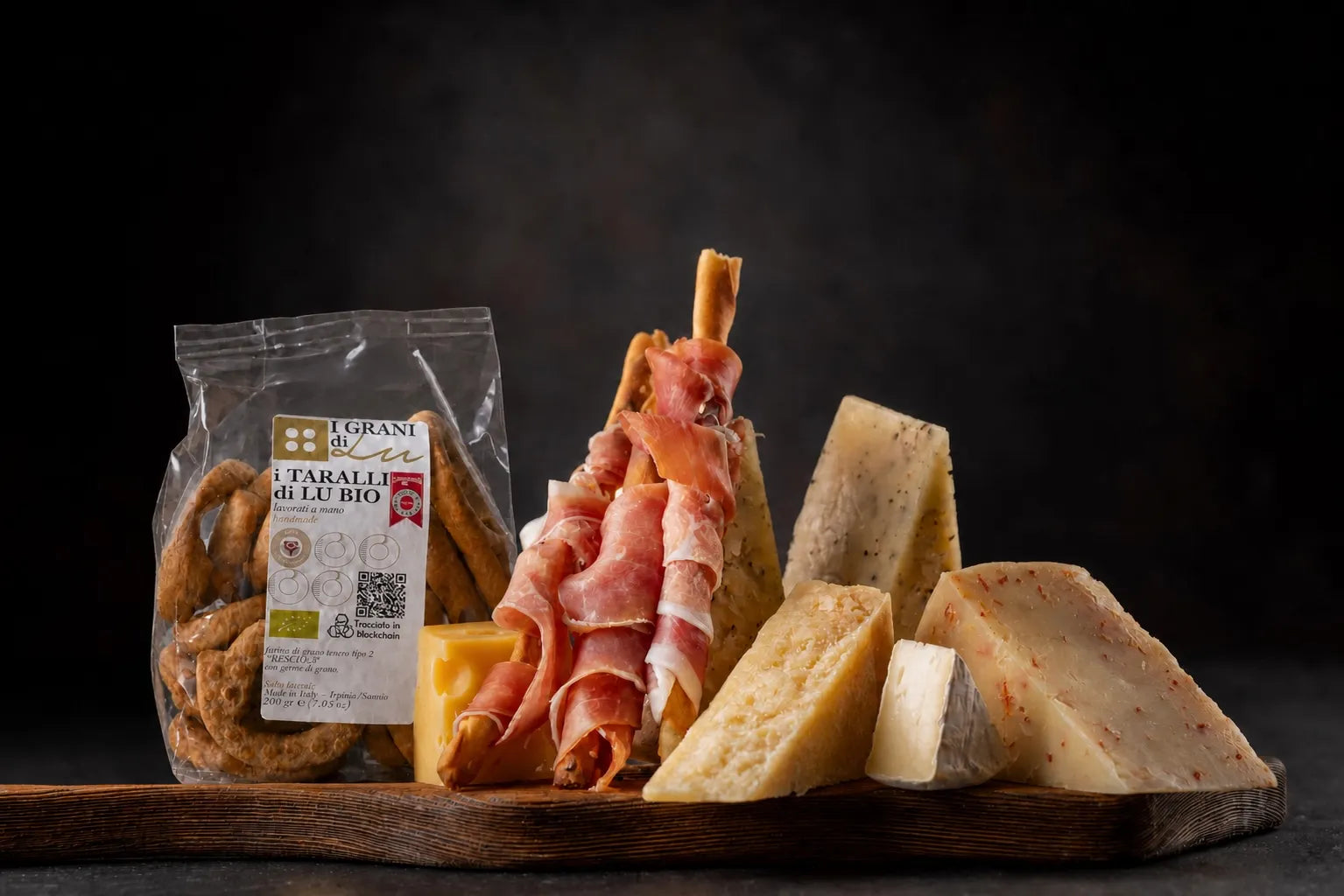 Taralli di Lu Bio con grissini avvolti nel prosciutto e assortimento di formaggi su tagliere.